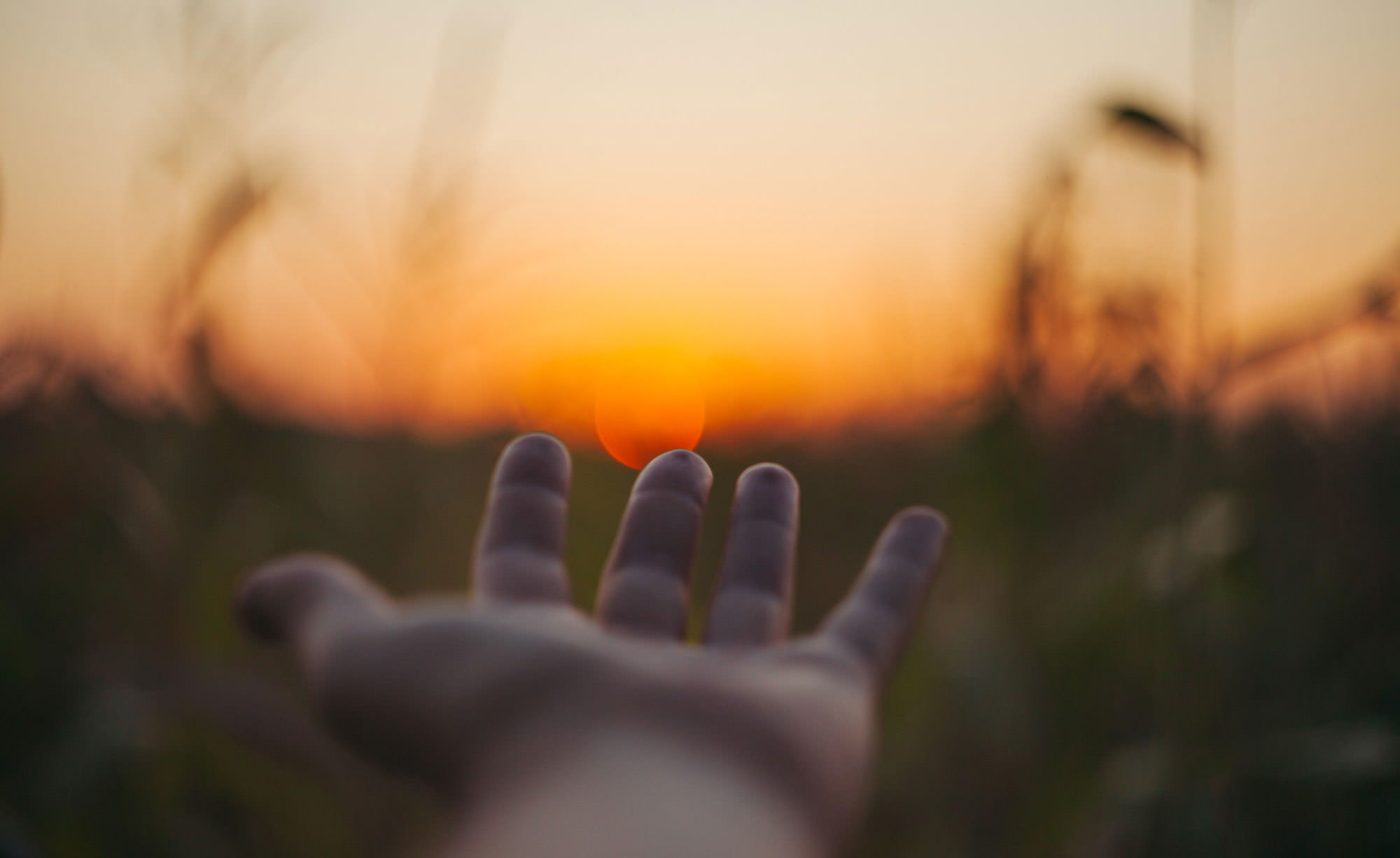 Ausgestreckte Hand in der Ich-Perspektive an einem Feld bei Sonnenuntergang